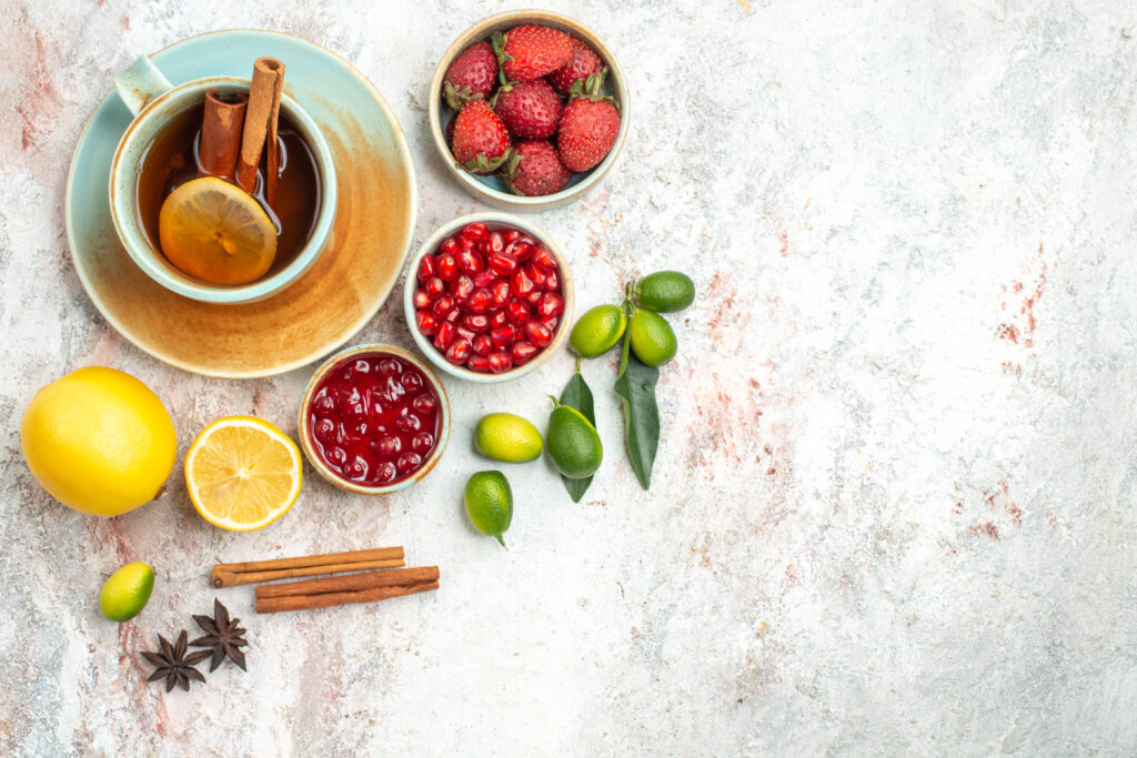 Tasse de thé avec une rondelle de citron et 
de la cannelle, entourée de fraises, graines 
de grenade, kumquats, confiture de fruits 
rouges et étoiles de badiane sur fond blanc